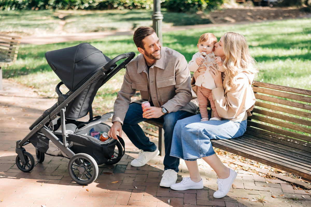 A family on a park bench beside an UPPAbaby Cruz