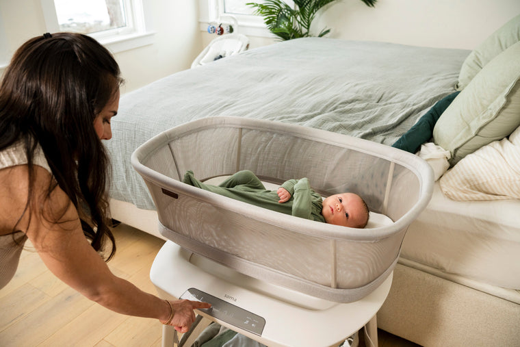A mother settling her newborn into an UPPAbaby Soma smart bassinet
