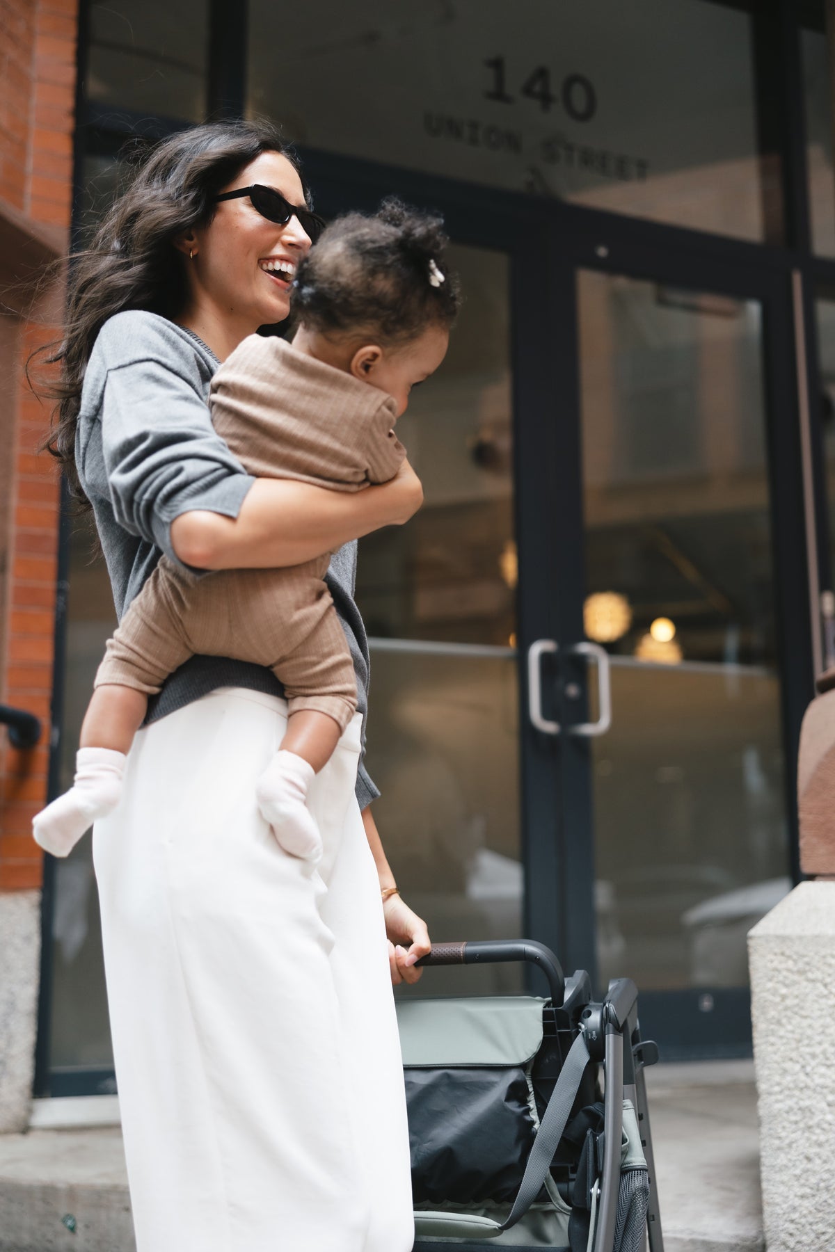 Mother lifting her baby out of a Kona in Evelyn, meadow green, outside a shopfront
