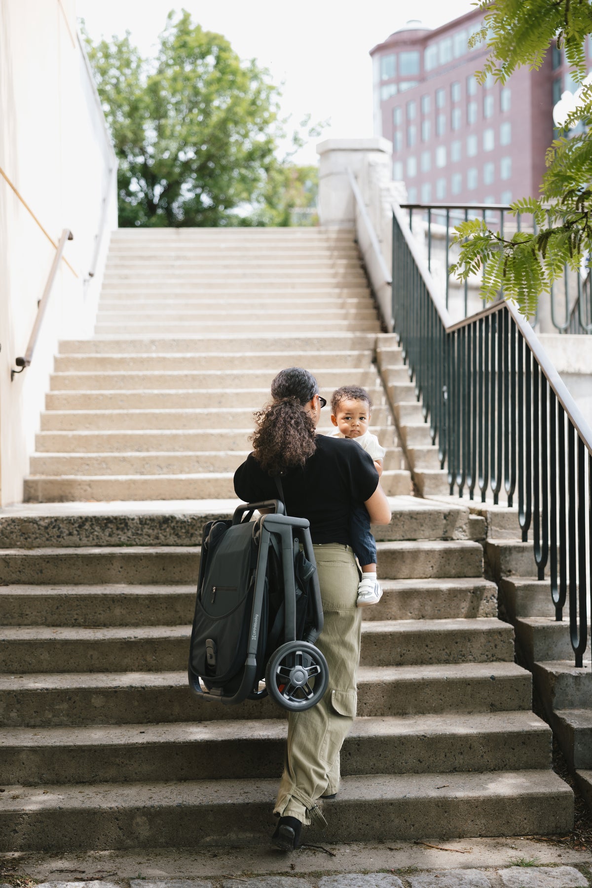 Carrying a folded Kona up a flight of stairs, toddler on the other hip